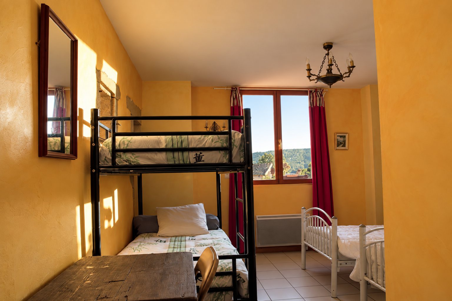 Chambre chaleureuse aux murs orange, équipée d'un lit superposé en métal, de deux lits blancs, d'un lustre et d'une fenêtre aux rideaux rouges.