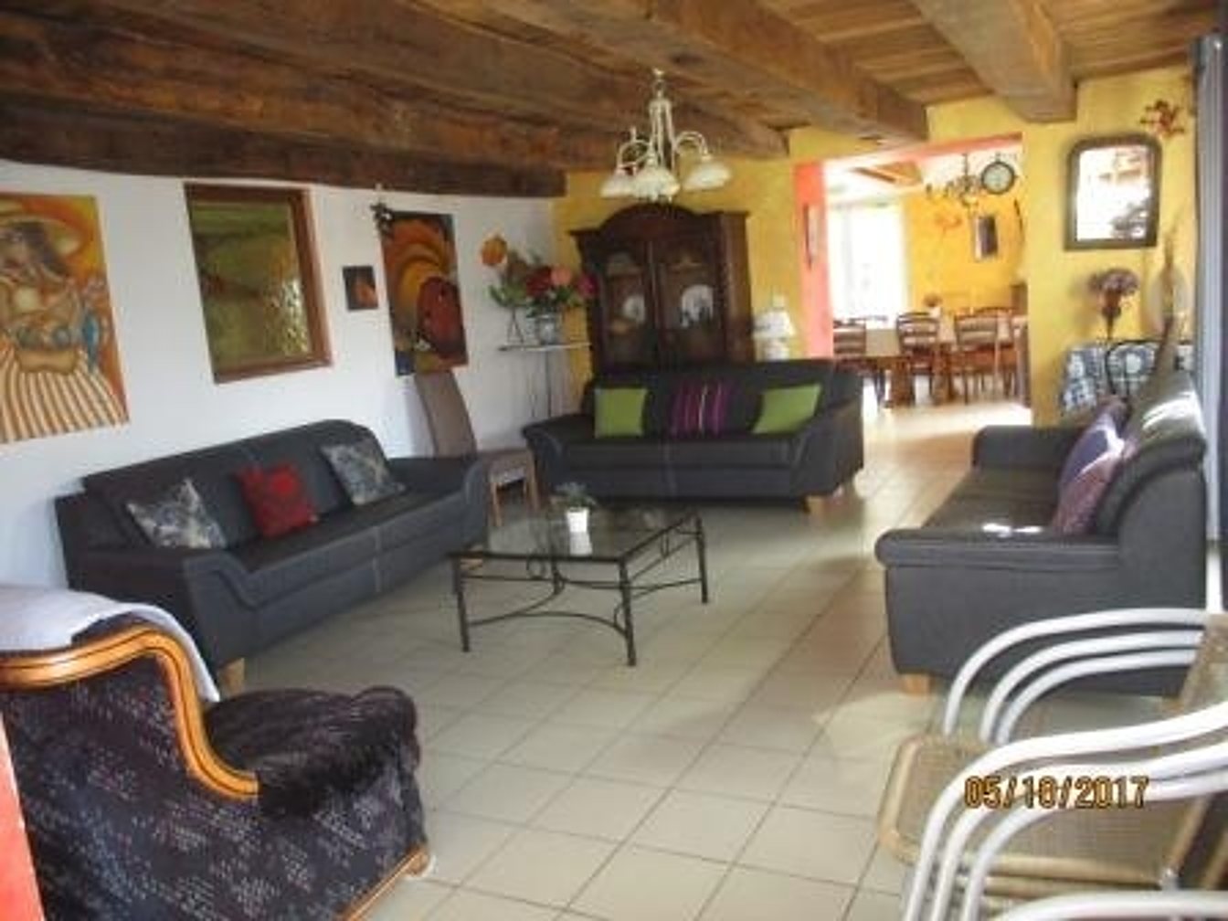 Un grand salon aux murs colorés et aux poutres apparentes, meublé de canapés en cuir sombre, d'une table basse en verre et d'une salle à manger en arrière-plan.