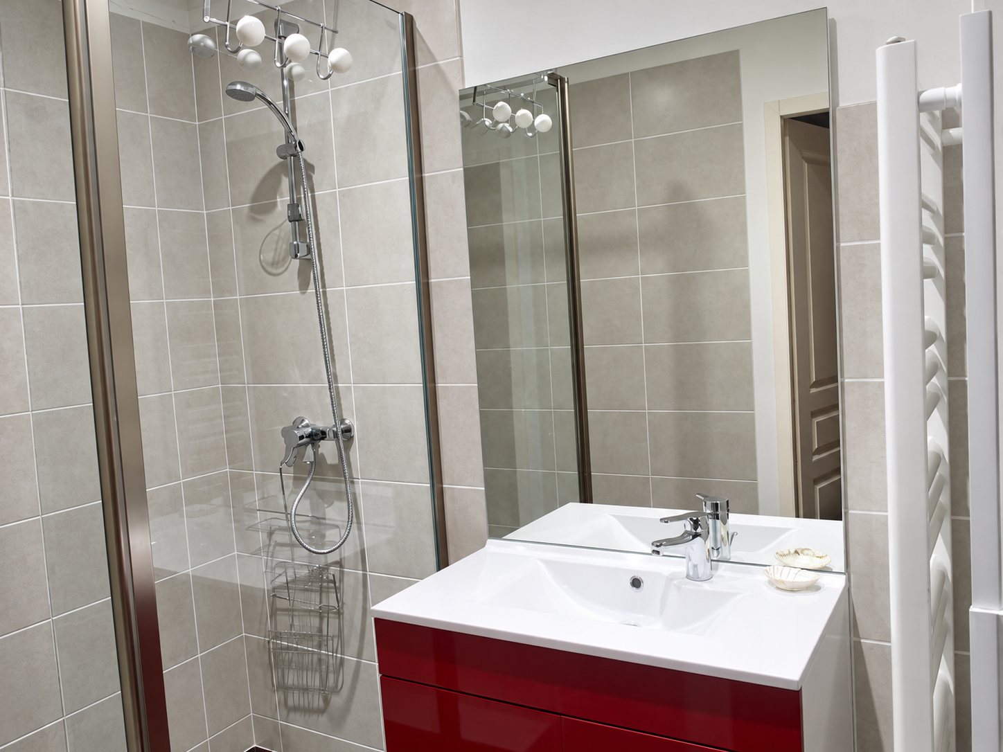 Salle de bain rénovée avec une douche vitrée carrelée en beige, un meuble vasque rouge, un grand miroir et un sèche-serviettes blanc.