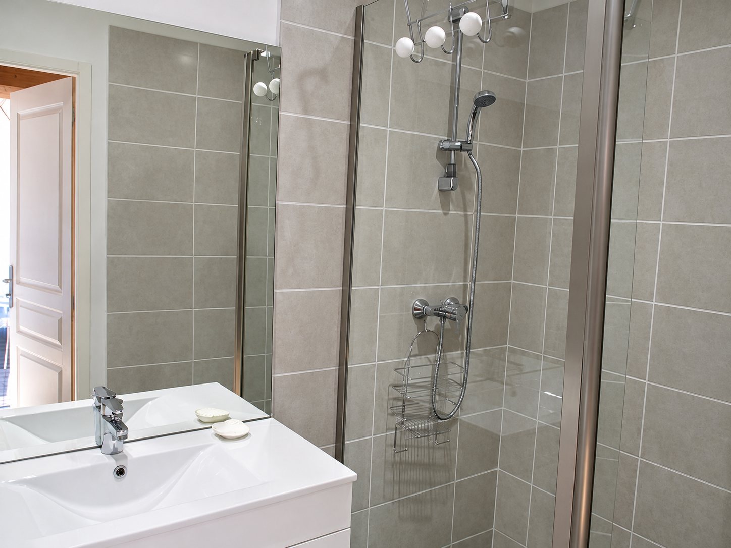 Salle de bains rénovée avec une douche à carreaux gris, une paroi vitrée, un meuble vasque blanc et un grand miroir.