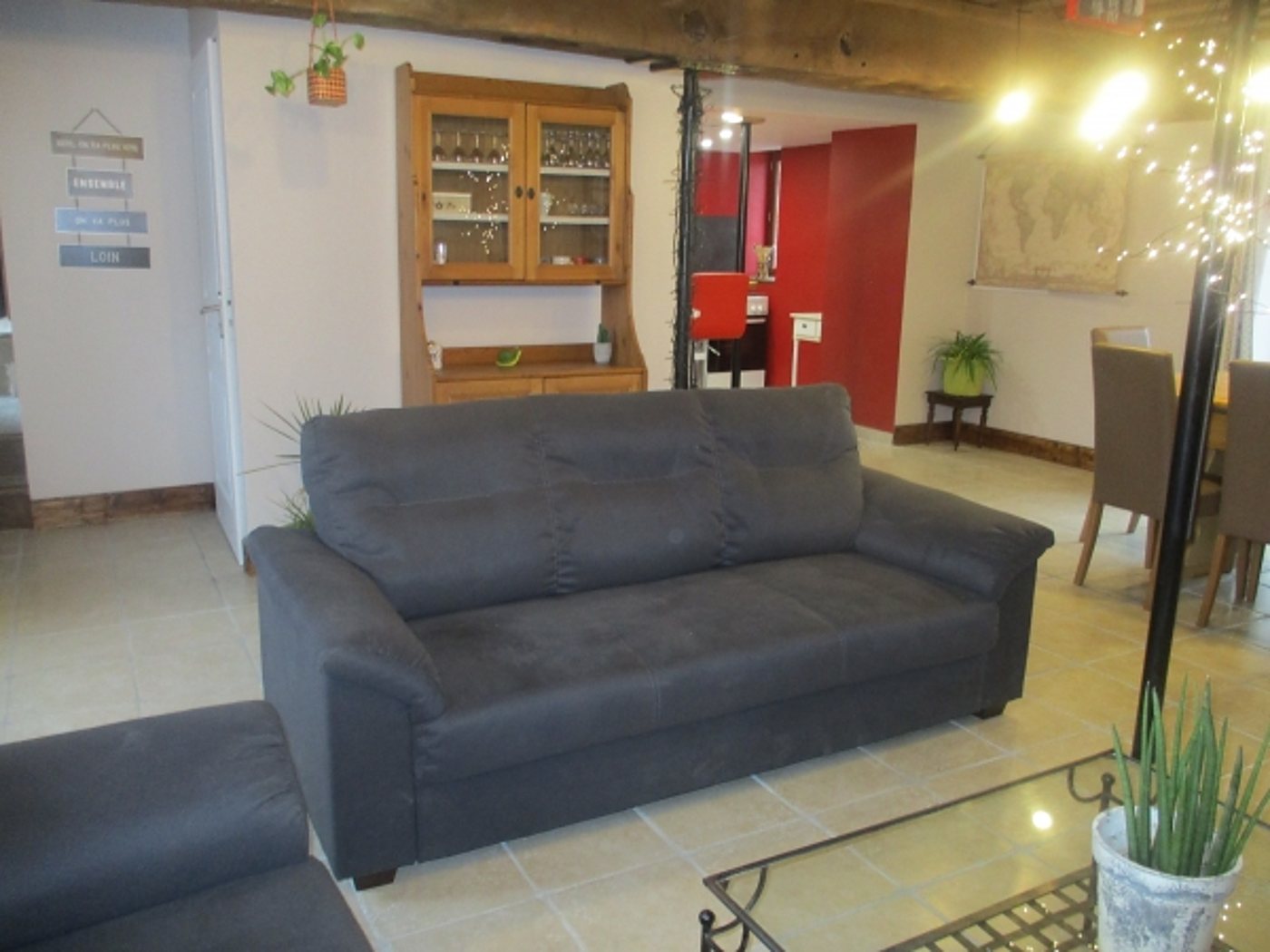Un salon lumineux avec un canapé gris anthracite, un buffet en bois, une table à manger et un sol en carrelage clair.